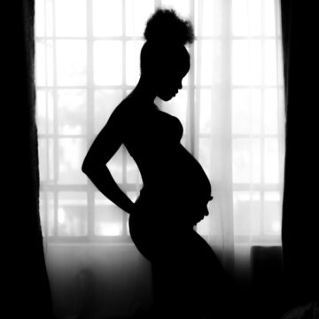 a silhouette of a pregnant woman in front of a wide window in a dark room