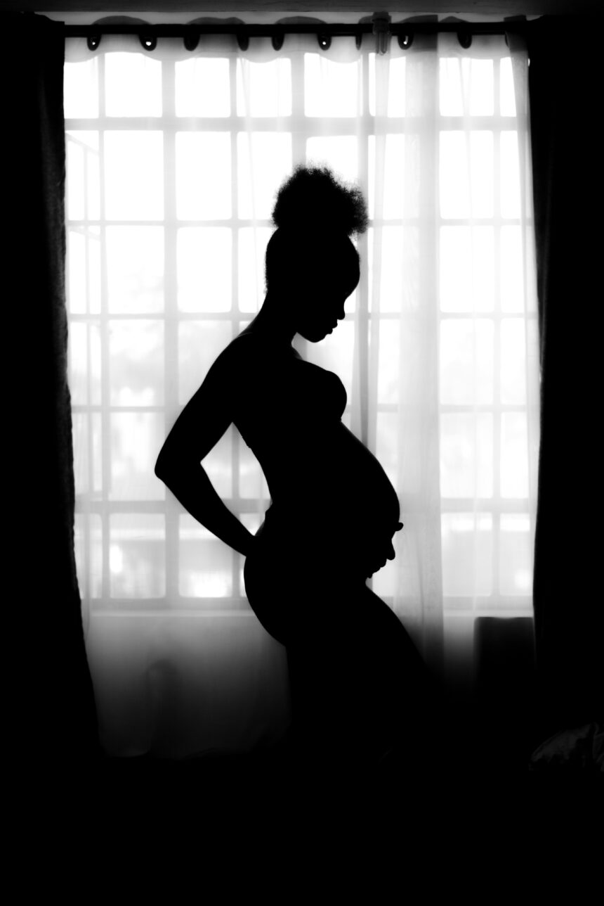 a silhouette of a pregnant woman in front of a wide window in a dark room