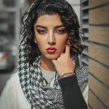 A photo of a Palestinian woman wearing a kuffiyah. She has brown curly hair and smokey eye makeup on
