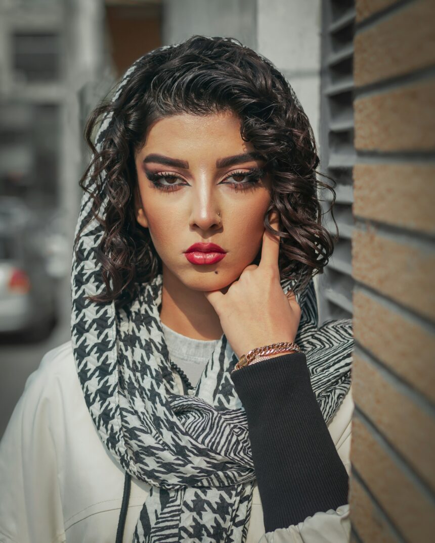 A photo of a Palestinian woman wearing a kuffiyah. She has brown curly hair and smokey eye makeup on