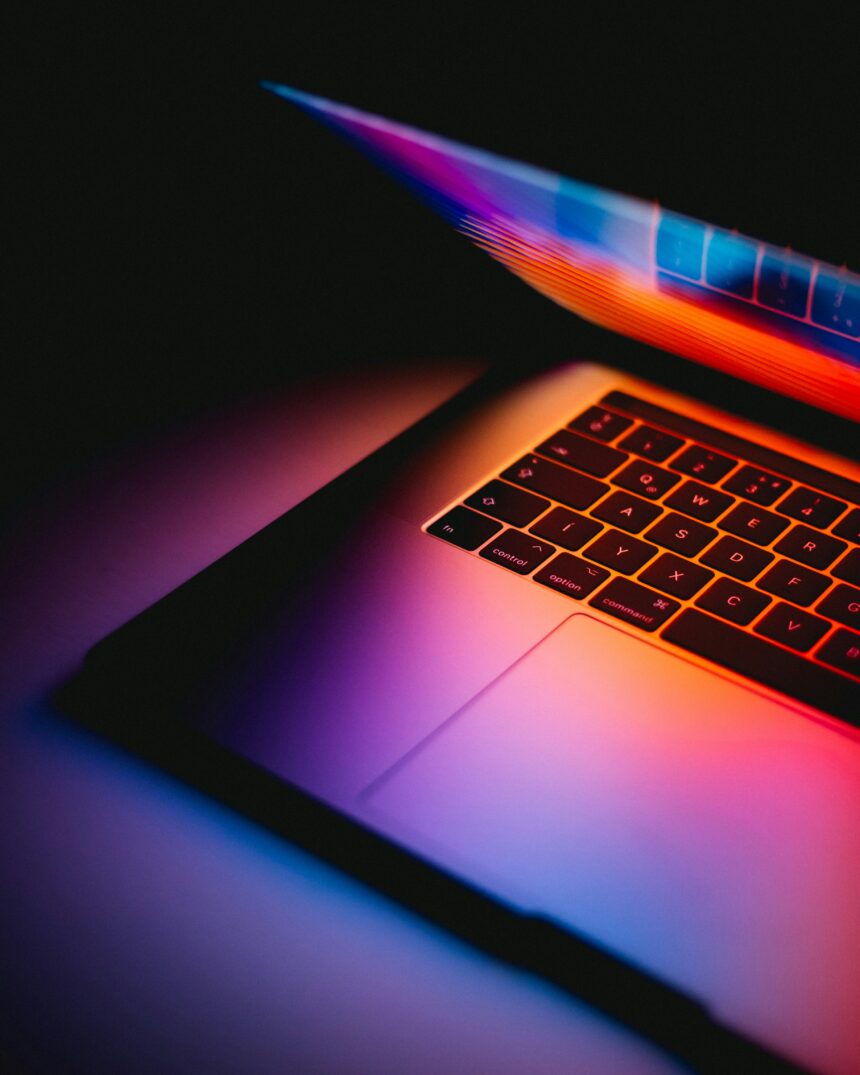 andras-vas-Bd7gNnWJBkU-unsplash a photo of a sleak laptop in a dark room. The laptop is closed to almost a 45 degree angle to reflect the light onto the keyboard and table