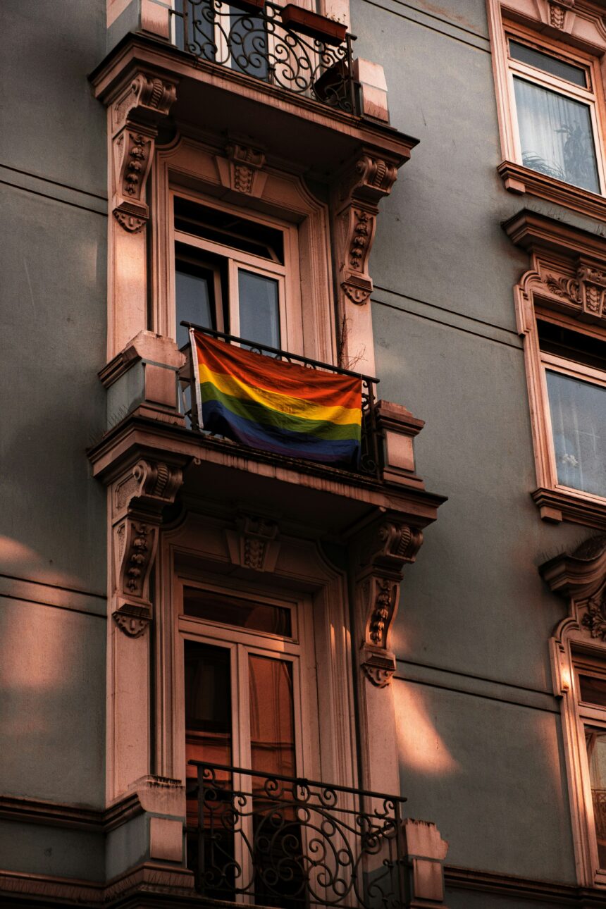 moritz-kindler-HyYlDsI_2vU-unsplash photo of a pride flag hanging from a building in s European city